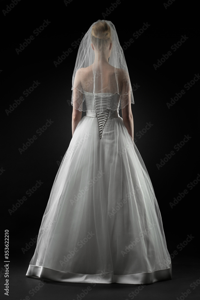 Bride in a beaituful long white wedding dress and lace bridal veil, back view. Black background Bride in a beaituful long white wedding dress and lace bridal veil, back view. Black background