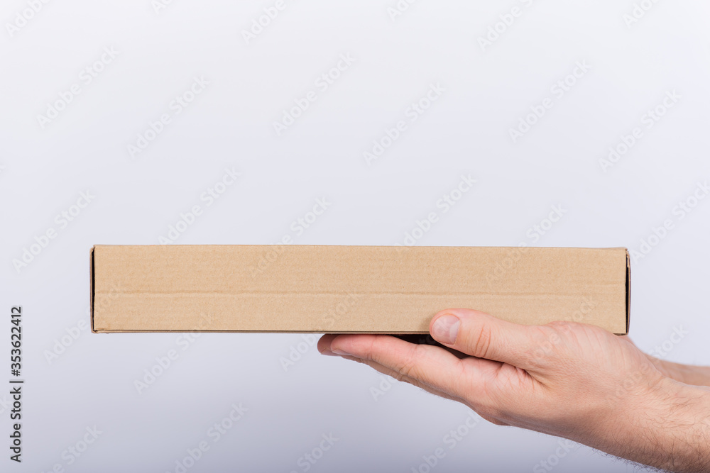 Flat cardboard box in male hands. Delivery of parcels. Side view.