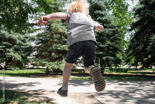 A little boy jumps far ahead in a park among the trees. View from the back