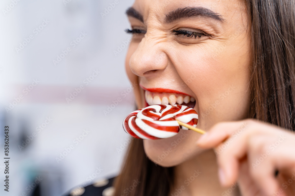 Woman bites lollipop with white healhy teeth. Beautiful lady with candy.