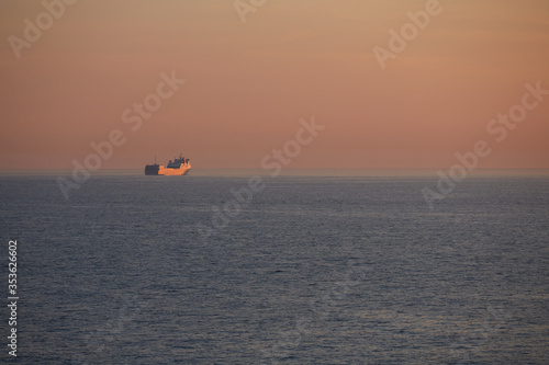 Commercial cargo ship sailing alone across North Sea in golden dusk light