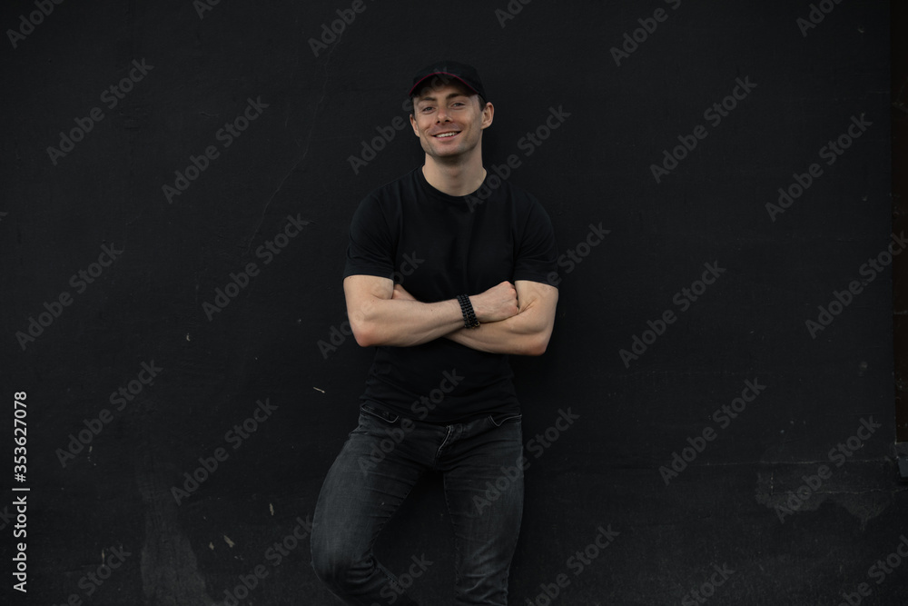 Stylish man with crossed arms standing leaning on black wall