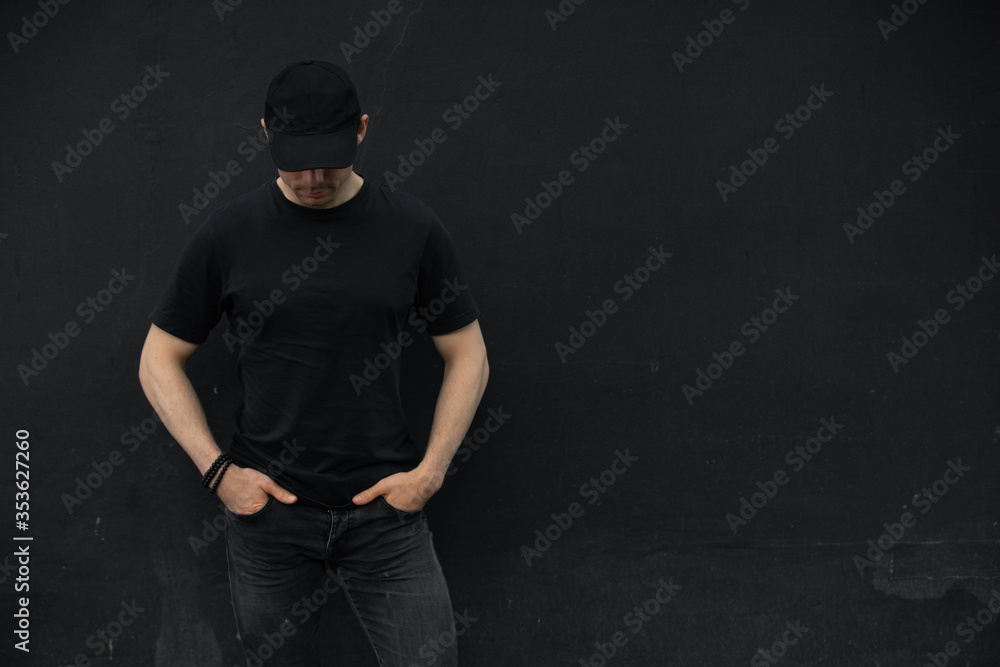 Man in cap and blank t-shirt standing against black wall Man in cap and blank t-shirt standing against black wall
