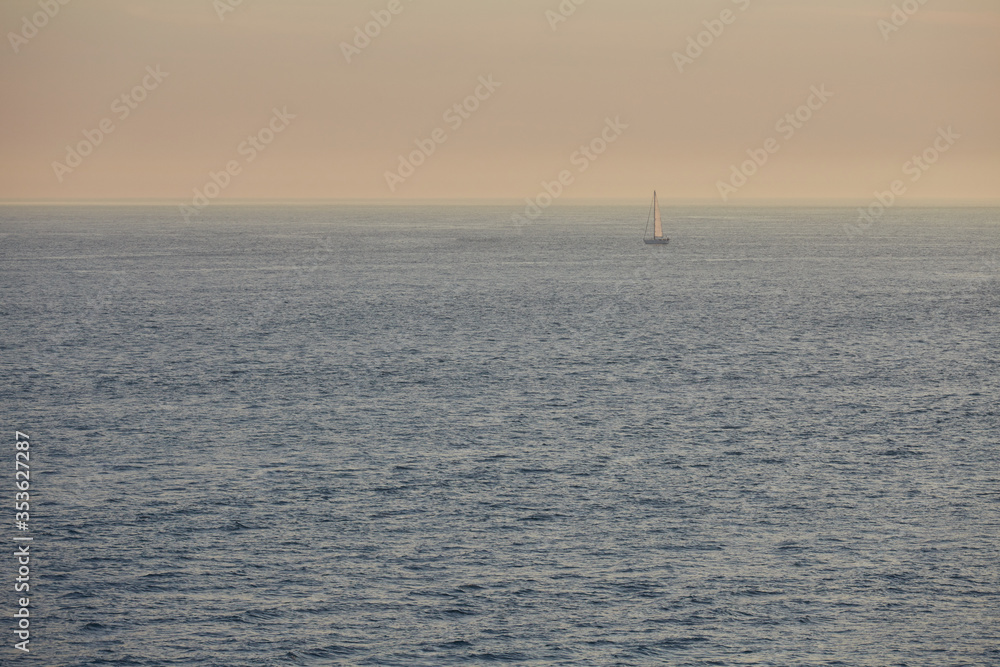 Obraz premium Sail boat sailing alone across vast sea in moody dusk light