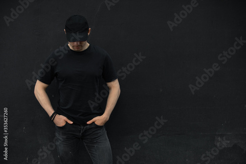 Man in cap and blank t-shirt standing against black wall