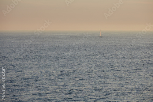 Sail boat sailing alone across vast sea in moody dusk light