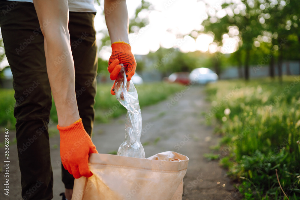 Fototapeta premium Men hand collects plastic trash for cleaning in the park. Volunteer wearing protective gloves collects bottle plastic. Environmental protection, ecological concept. Waste recycling.