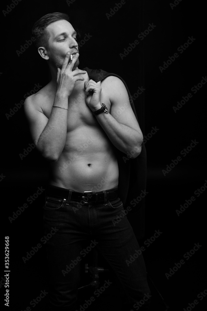 Fototapeta premium Sports guy in a jacket smokes a cigarette on a black background