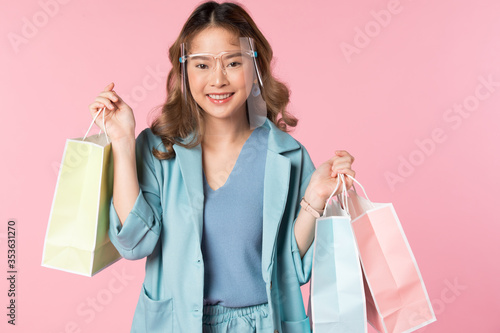 Beautiful Asian women wear face shield to protect virus and hold shopping bags. isolated over pink studio background.  shopping concept and life style photo