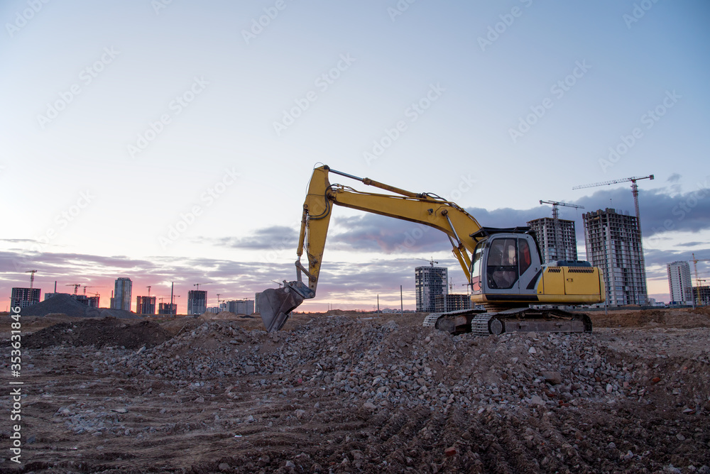 Excavator working at construction site on sunset background. Backhoe digs gravel and concrete crushing. Recycling old concrete from demolition at a landfill for the disposal of construction waste Excavator working at construction site on sunset background. Backhoe digs gravel and concrete crushing. Recycling old concrete from demolition at a landfill for the disposal of construction waste