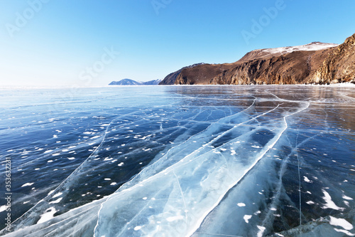 Beautiful winter landscape of Siberian Baikal Lake with smooth blue ice with cracks near the coastal cliffs on a sunny day. Natural background