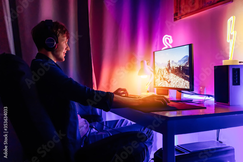 gamer plays online video games in the first person on his personal computer, sitting in a room with neon lights. Online cyber sport championship.