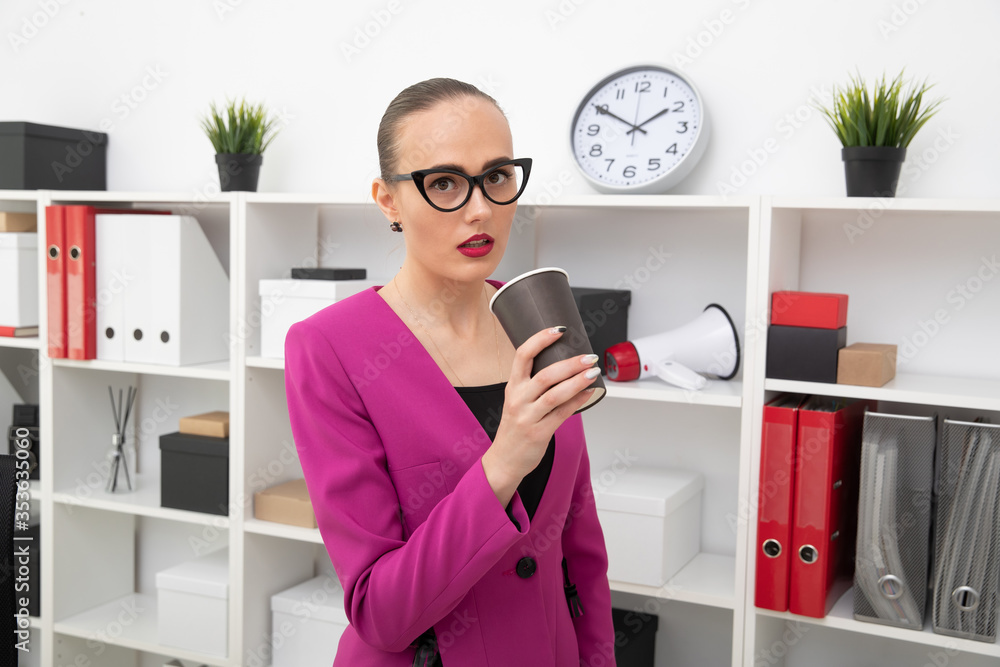 Portrait of a girl in a skirt and pink jacket who drinks coffee from a plastic cup. A break in the work day in the office Portrait of a girl in a skirt and pink jacket who drinks coffee from a plastic cup. A break in the work day in the office