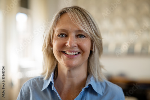 Free Download Authentic close up of an attractive mature blond hair woman with blue eyes is smiling in camera in living room at home.	 - GFXLoad