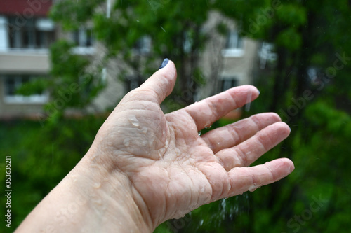 Rain drips on an elderly woman's hand. Rain drops bounce off. Blurred background. © Olga