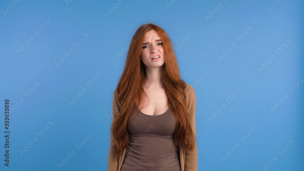 Ginger model in brown t-shirt and cardigan. She looking disappointed and showing blah blah blah sign, posing against blue background. Close up Ginger model in brown t-shirt and cardigan. She looking disappointed and showing blah blah blah sign, posing against blue background. Close up