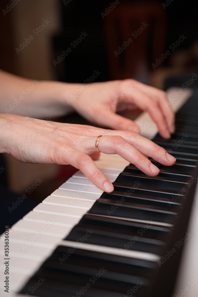 Closeup of the hands of a young woman playing the piano. The girl musician is preparing to start playing a musical composition. Synthesizer or classical piano with classic keys. Music concept