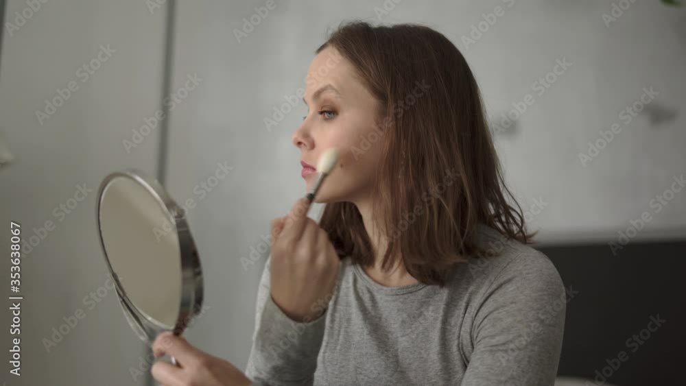 Woman holding makeup brush applying makeup on her face Woman holding makeup brush applying makeup on her face