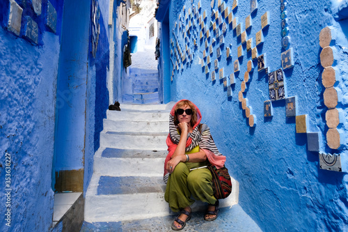 Alone female tourist sitting on the street stairs in blue city Chefchaouen, Morocco.