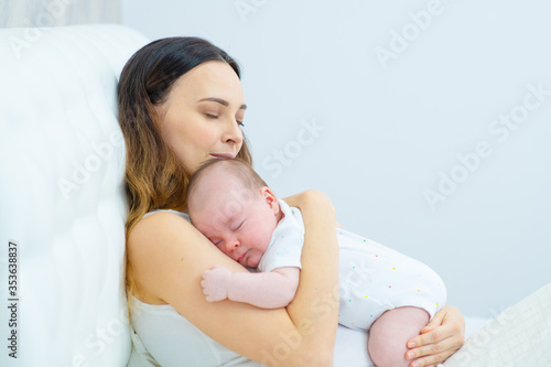 A newborn baby sleeps on her mother’s chest. Mom holding a baby in her arms sleeping leaning back in bed