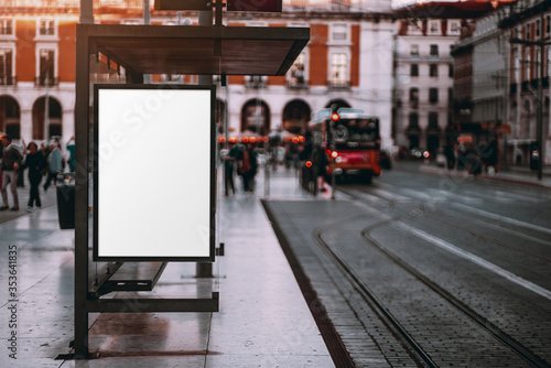 A blank advertising billboard placeholder template on the city street; an empty mock-up of an outdoor poster on a tram stop in Lisbon; a white vertical mockup of an urban banner on the bus stop