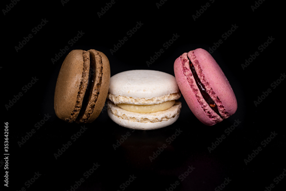 Colored macaroons, French cookies isolated on a black background. Brown white and pink cookies, biscuits Colored macaroons, French cookies isolated on a black background. Brown white and pink cookies, biscuits