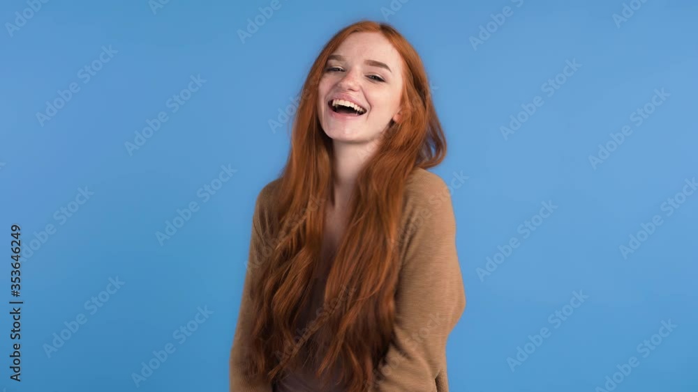 Red-haired model in brown t-shirt and cardigan. Clenched her fists and showing yes sign by hands , smiling while posing on blue background. Close up Red-haired model in brown t-shirt and cardigan. Clenched her fists and showing yes sign by hands , smiling while posing on blue background. Close up
