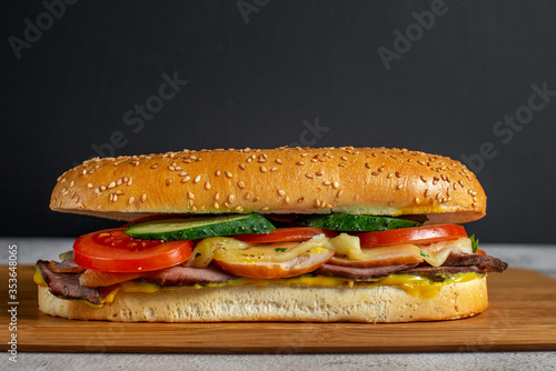 Sandwich with sesame bun, cheese, ham, fresh vegetables and mustard