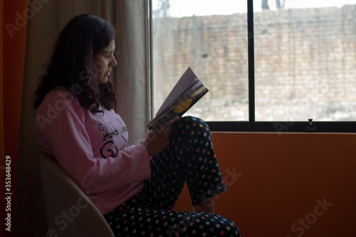 Woman in armchair sitting in front of the window reading a book