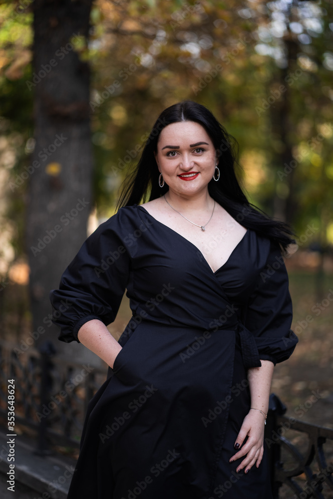 Autumn fashion outdoor. The girl with red lips in fashionable stylish black dress, autumnal lifestyle on the background of blurry yellow-green trees in the park. Vertical Autumn fashion outdoor. The girl with red lips in fashionable stylish black dress, autumnal lifestyle on the background of blurry yellow-green trees in the park. Vertical