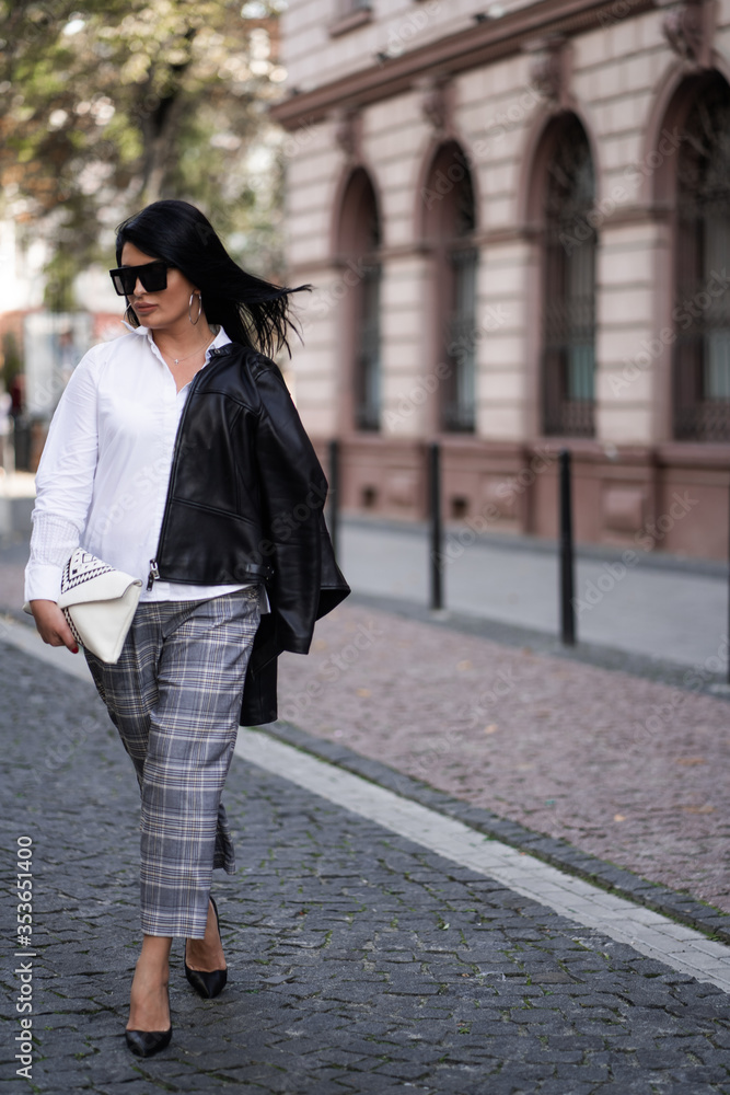 Fototapeta premium Autumn fashion outdoor. The girl in fashionable stylish white shirt , pants, jacket and sunglasses, autumnal lifestyle on the background of blurry yellow-green trees in the park. Vertical