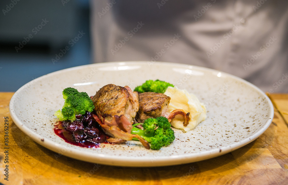 meat medallions in bacon with broccoli and cherries on a light plate beautifully canned meat medallions in bacon with broccoli and cherries on a light plate beautifully canned
