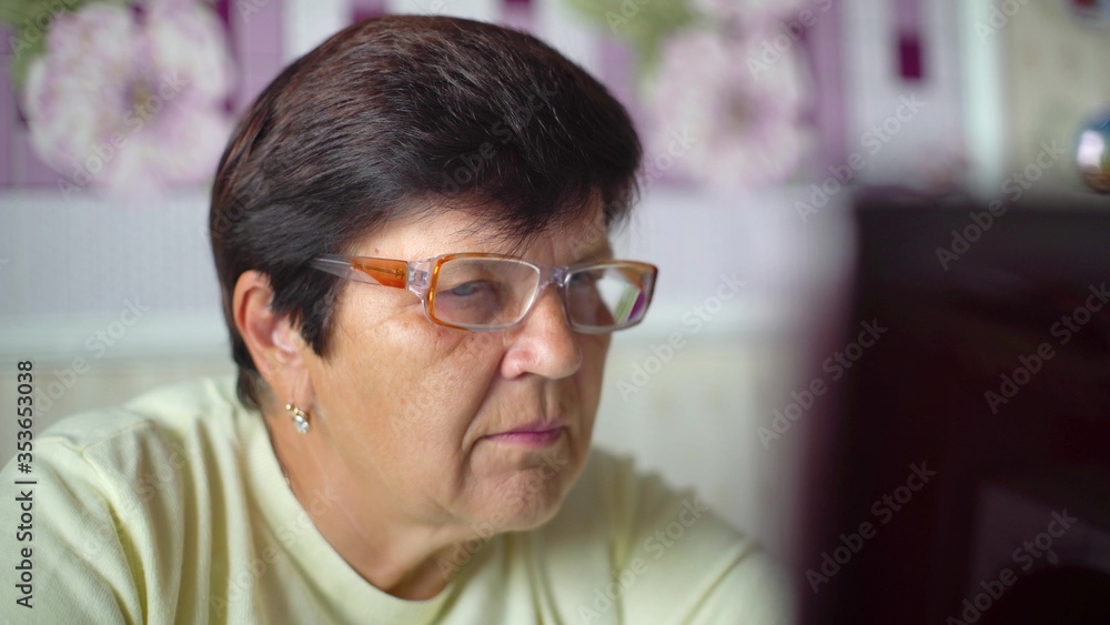 Senior old woman in eyeglasses surfing internet on laptop at home closeup Senior old woman in eyeglasses surfing internet on laptop at home closeup