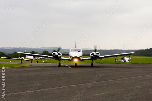 Εκτύπωση καμβά Two twin engine aircraft Piper PA 34 Seneca taxiing at Holzminden-Höxter airport with a wind farm on the background