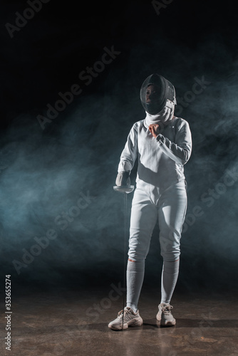 Fencer adjusting fencing mask on black background with smoke