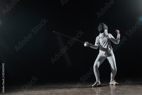 Fencer training with rapier under spotlight on black background