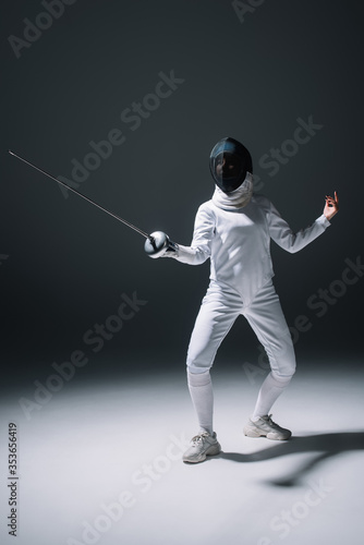 Fencer in fencing mask training with rapier on white surface on black background