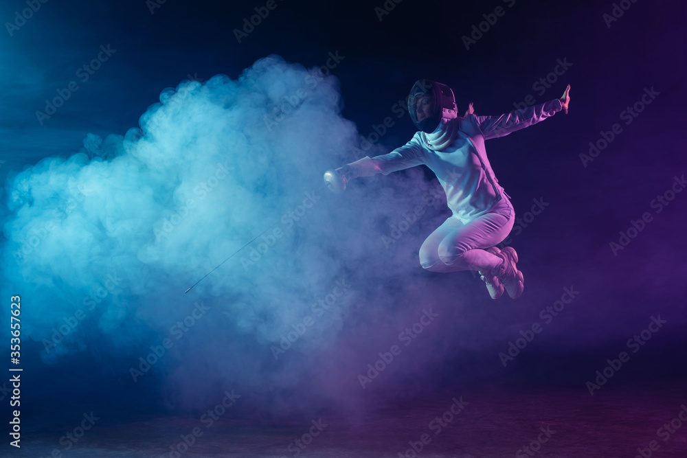 Fencer jumping while exercising with rapier on black background with lighting and smoke