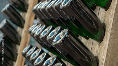 Wooden racks with filled green bottles of champagne during traditional bottle fermentation waiting for the next manual bottle rotation to proceed with the maturation process. 