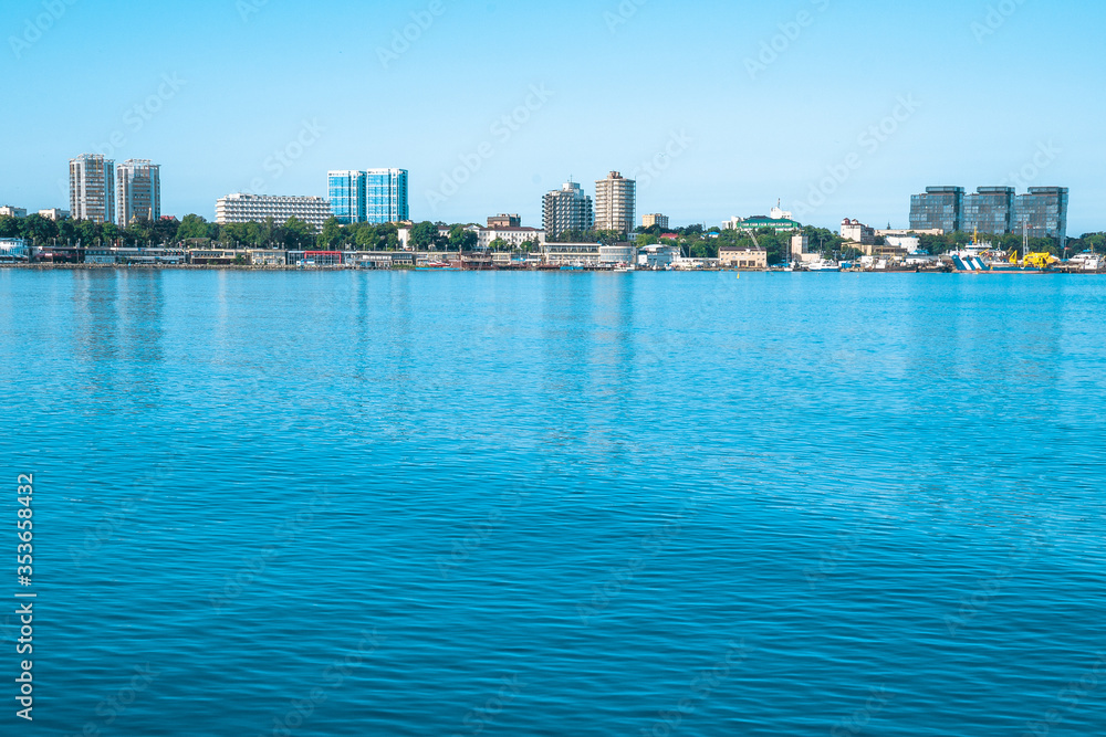Beautiful city with tall buildings on the shores of the blue sea. Coastline with houses on a clear day.