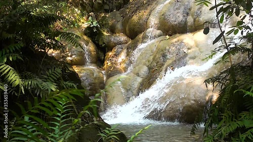 Slow motion, water flowing over round rocks, shadows and sun, protective feeling, foliage, ferns