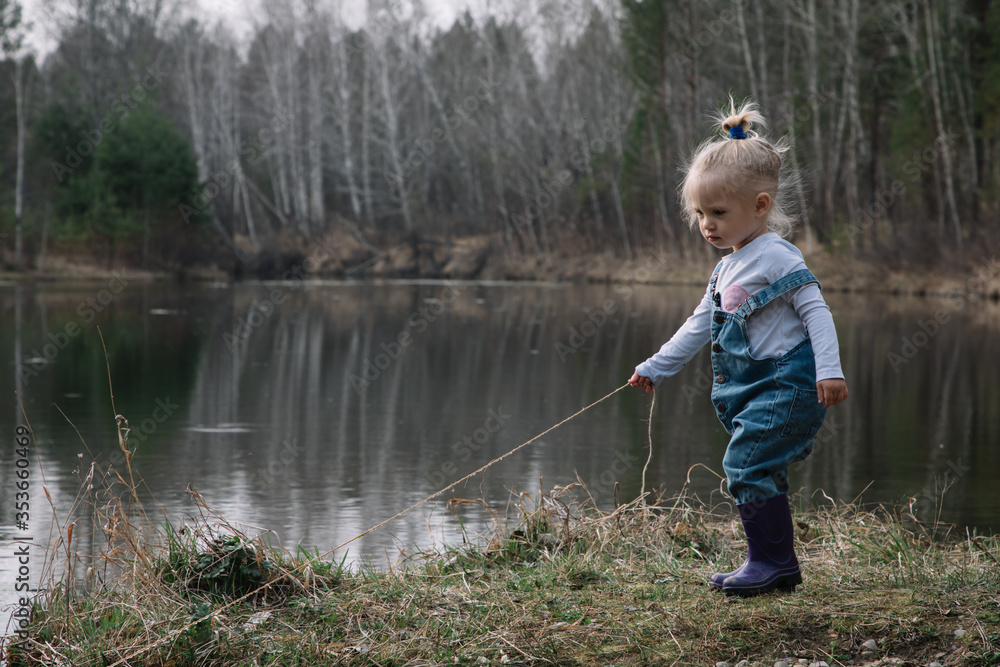 Little girl in rubber boots catches and feeds fish on the river in a jar
