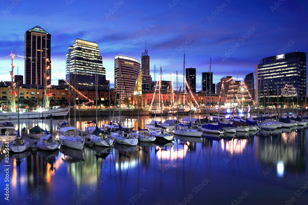 Obraz premium Yachts at the harbor of Buenos Aires, at twilight. Water reflections and modern buildings at the background. Puerto Madero, Buenos Aires, Argentina.