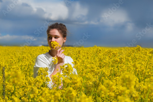 Brunette girl in rapeseed field summer time, facing side way blue sky background. Happy beautiful young woman enjoys smell of blooming rapeseed field full of joy and happiness. Concept of freedom