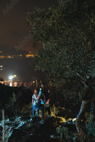 Two tourists on top of the mountain. Climbing, hiking trail. View of the night city. Romantic setting. Couple in love. Active lifestyle. The best view. vertical photo. Vacation. Nerano, Italy