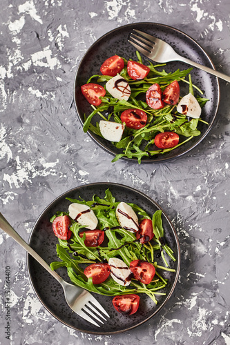 Caprese salad. Healthy meal with cherry tomatoes, mozzarella balls, spices, fresh arugula . Home made, tasty food. Concept for a tasty and healthy vegetarian meal. Top view 