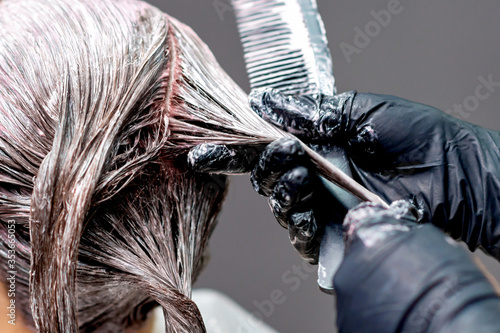 Hands of hairdresser are dyeing hair of woman, close up.