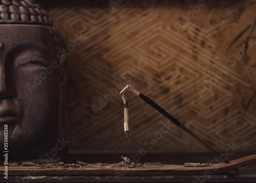 Burning single incense stick for meditation with Buddha on the background.
