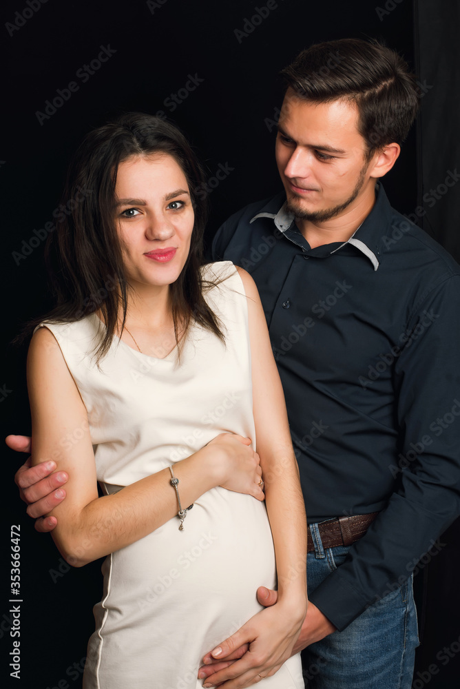 Happy pregnant wife and husband hugging on black background. The concept of a young family Happy pregnant wife and husband hugging on black background. The concept of a young family