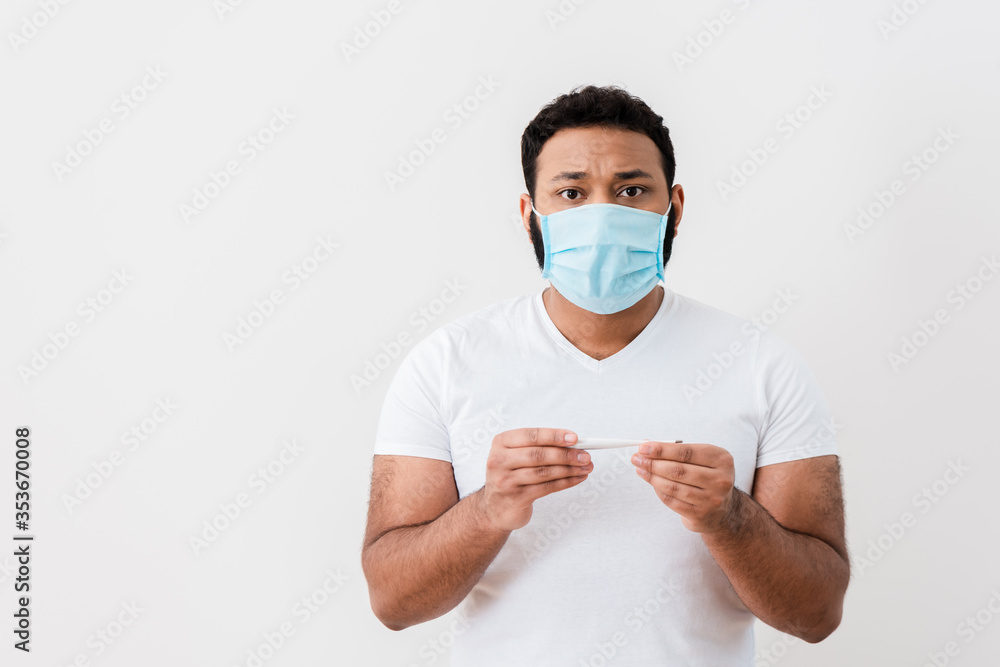 sick african american man in medical mask holding digital thermometer near white wall sick african american man in medical mask holding digital thermometer near white wall